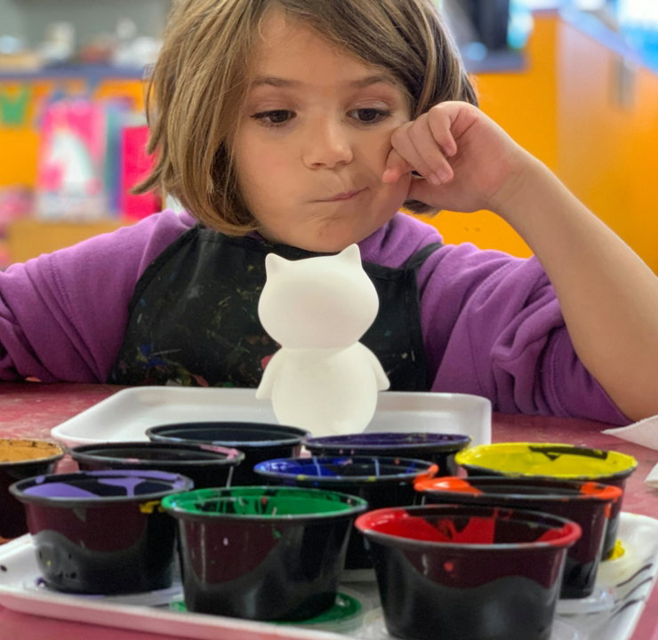 child sitting in front of table with white animal toy and containers of paints